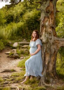 Stunning expecting mom leaning against a tree.