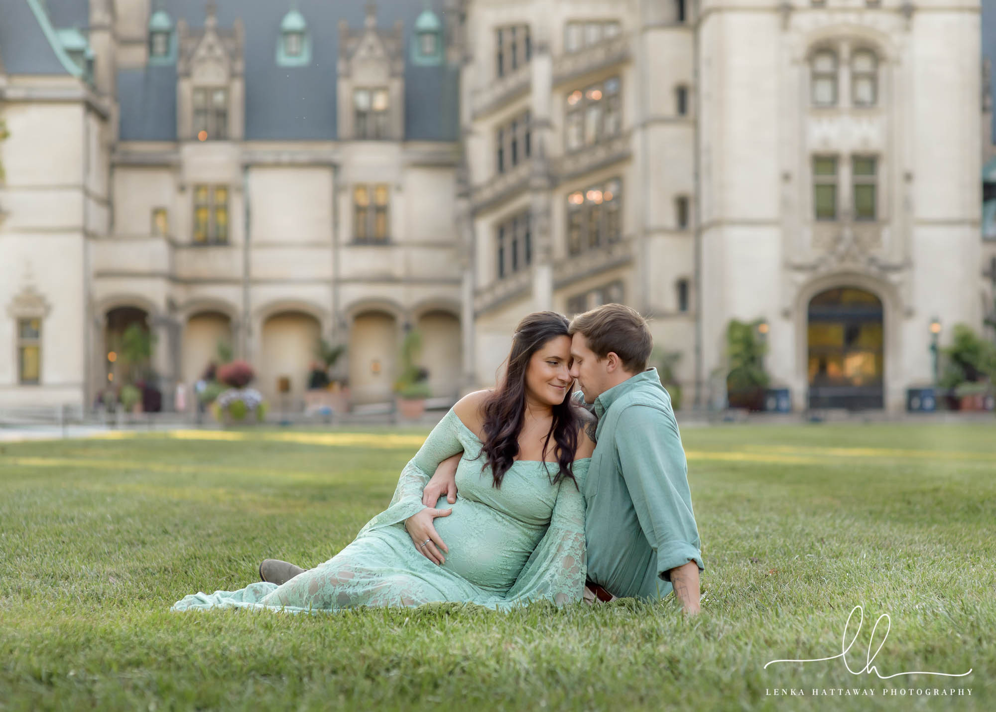 Expecting couple sitting down in front of the Biltmore house.