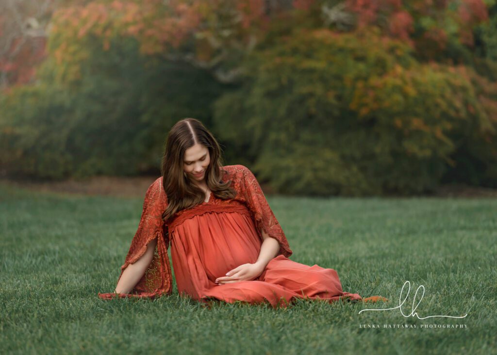 Mom to be sitting on grass holding her belly.